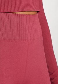 Růžová dlouhá rukávová ribbed halenka s krátkým střihem a texturovaným pasem, vyrobená z měkké a pružné tkaniny.
