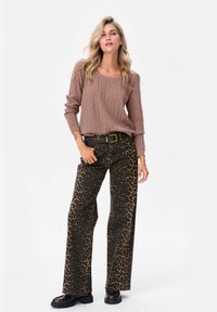 Bruine gebreide trui met lange mouwen, gecombineerd met hoge wijde broek met een luipaardprint. Zwarte stevige laarzen maken de look compleet.