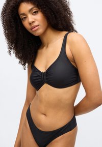 Černý vršek plavek s širokými ramínky a střihem se středním nařasením, doplněný o odpovídající spodní díl plavek s nízkým pasem. Hladká, elastická látka.