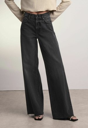 Brede zwarte jeans met een hoge taille, gemaakt van denim. Beschikt over een rafelige zoom en een klassieke vijf-pocketstructuur. Combineer met zwarte sandaaltjes met bandjes.