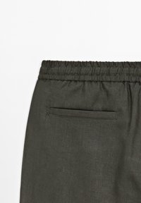 Pantaloni in lino verde scuro con vita elastica e texture arricciata, dotati di una sola tasca posteriore. Tessuto morbido con una leggera lucentezza.