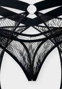 Μαύρα δαντελένια εσώρουχα με γεωμετρικά κοψίματα, δίχτυνα πάνελ και μεταλλικό δαχτυλίδι στη μέση, παρουσιάζονται σε λευκό φόντο.