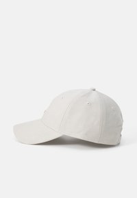 Light beige baseball cap with a smooth texture, curved brim, and ventilation eyelets, featuring a stitched logo on the front.