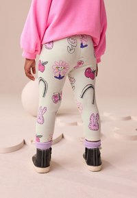 Leggings colorate in tessuto verde pastello a coste con motivi rosa di fiori, frutta e coniglietti. Abbinati a stivali neri e felpa rosa.
