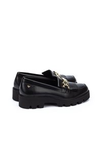 Mocasines de cuero negro con suela gruesa, que presentan un detalle de cadena dorada y un diseño plisado en la parte frontal. Textura suave con un branding mínimo.