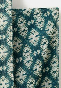 Lekka tkanina z niebiesko-zielonym i białym wzorem tie-dye kwiatowym, ukazująca przeszycie oraz miękką, płynną fakturę.