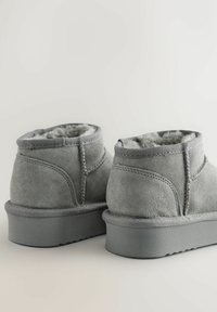 Grå suede ankelstøvler med blødt pelsfor, solid sål og kontrasterende syninger. Rundet form, lavskåret design.