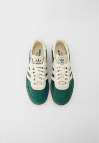 Gröna och krämfärgade Adidas-sneakers i mocka och läder, med tre krämfärgade ränder, gummisula och snörning.