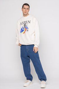 Sudadera blanca con el texto negro "ASPEN", un gráfico de montaña colorido y el detalle "1999", combinada con pantalones de mezclilla azules y zapatillas beige.