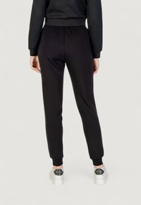 Czarne dresy z elastycznym pasem i dopasowanymi mankietami, wykonane z miękkiego materiału. Noszone z białymi trampkami z czarnym akcentem na pięcie.