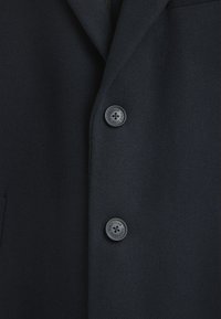 Mörkblå ullblandad jacka med kraag, som har två svarta knappar och en sidficka. Slät textur med en skräddarsydd passform.