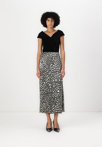 Schwarzes Samtoberteil mit einem verdrehten Vorderteil, kombiniert mit einem langen schwarz-weißen gedruckten Rock mit floralem Muster. Schwarze High Heels.
