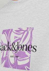 Grå bomulds t-shirt med et lilla blomsterdesign og "Jack & Jones" tekst samt "EST. 1990" nedenunder i sort. Rund halsudskæring, korte ærmer.