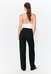 Czarne spodnie o szerokich nogawkach wykonane z gładkiej tkaniny, z wysokim pasem i subtelnymi zakładkami z przodu, zestawione z białym, bezramiączkowym topem.