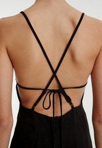 Schwarzes Kleid mit einem tiefen Rückenausschnitt, dünnen, gekreuzten Trägern und einer gebundenen Detail. Hergestellt aus glattem Stoff mit matter Textur.