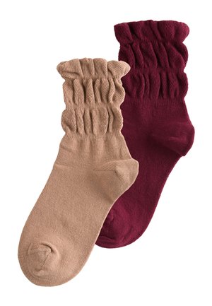 To par sokker: den ene er beige med en ribbet manchet, den anden er dyb bordeaux med et lignende design, begge lavet af blødt stof.