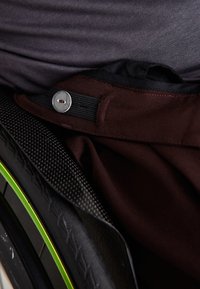 Gros plan sur un tissu marron avec un bouton métallique, positionné près d'une roue de fauteuil roulant texturée noire et jaune.