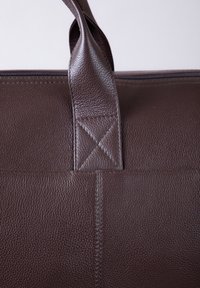 Brown leather bag with a textured finish. Features reinforced stitching and two top handles. Zipper closure along the top edge.