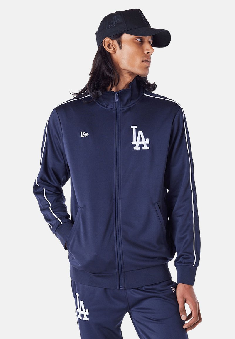 Navy Zip-Up Trainingsjacke aus glattem Stoff, mit weißen Streifen an den Ärmeln und einem weißen "LA"-Logo auf der Brust.