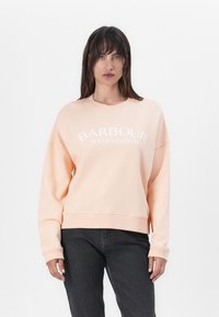 Őszibarack színű pulóver, puha anyagból készült, kerek nyakkivágással, ejtett vállakkal, és fehér "BARBOUR INTERNATIONAL" felirattal az elején.