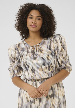 Blouse fluide en tissu texturé multicolore avec des motifs abstraits en beige, gris et noir, dotée d'un col à nouer et de manches bouffantes.