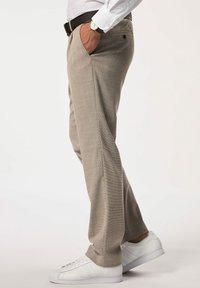 Hellbraune Hose mit strukturiertem Muster, seitlichen Taschen und schlanker Passform, kombiniert mit weißen Sportschuhen.