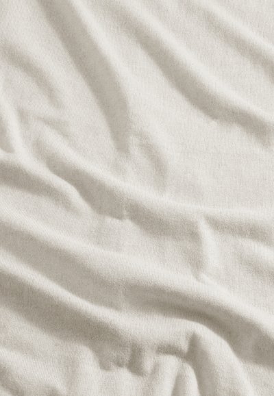 Tissu beige clair et doux avec une texture tissée visible et des plis naturels créant de légères ombres sur la surface.