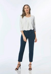 Witte, losse blouse met een ronde hals en plooien, gecombineerd met marineblauwe tapered broek en zwarte sandalen met hakken en banden.
