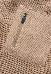 Beige gestrickter Pullover mit strukturiertem Muster, einem glatten Einsatz mit einer Reißverschlusstasche und gerippten Akzenten im unteren Bereich.