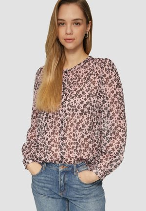 Chemisier rose transparent avec imprimé léopard marron, col rond et boutons sur le devant. Manches longues avec épaules froncées, associé à un jean bleu.
