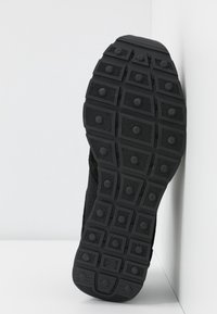 Semelle de chaussure de sport noire avec une surface en caoutchouc texturée. Présente des motifs rectangulaires et circulaires pour l'adhérence, avec un bord renforcé.