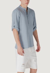 Maglietta henley azzurro chiaro con scollatura tonda, tre bottoni e maniche arrotolate, abbinata a pantaloni corti bianchi strappati.