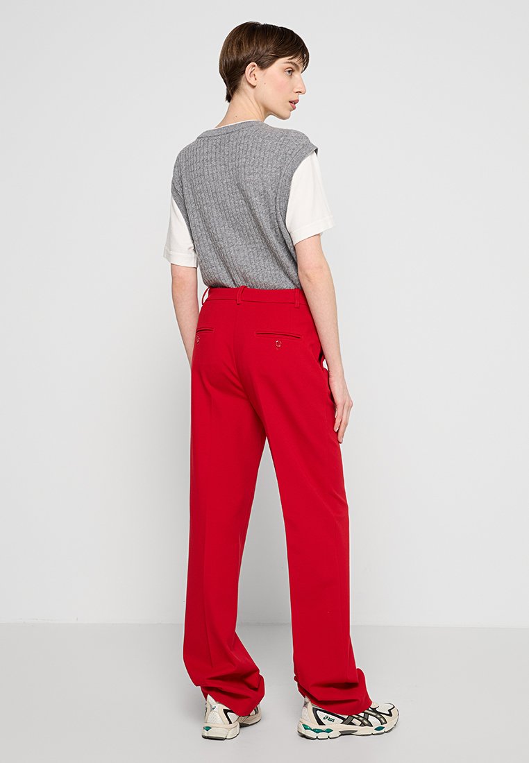 Gilet a costine grigio su una maglietta bianca abbinato a pantaloni rossi a vita alta. I pantaloni presentano tasche posteriori e un design dritto.