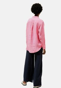 Camicia a righe rosa con maniche lunghe e polsini a bottone, vestibilità comoda e orlo arrotondato, abbinata a pantaloni larghi blu navy. Design semplice e casual.