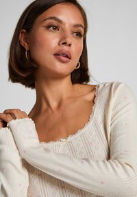 Μπλούζα μακρυμάνικη σε κρεμ χρώμα με ντεκολτέ διακοσμημένο με δαντέλα, featuring ροζ σχέδια καρδιών, υφή υφάσματος και εφαρμοστά μανίκια.