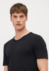 Schwarz kurzärmliges T-Shirt mit V-Ausschnitt-Design, hergestellt aus weichem Stoff mit glatter Textur. Einfaches und minimalistisches Erscheinungsbild.