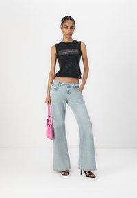 Svart ärmlös topp med strukturerad detalj, kombinerad med ljusblå vida jeans. Modellen håller en ljusrosa handväska och bär svarta klackar.