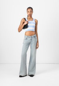 Blå og hvit stripete crop top kombinert med lyseblå flagrende jeans. Modellen holder en svart veske, og viser frem en uformell, moderne motestil.