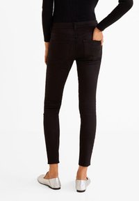 Jeans negros ajustados con una cintura de altura media y bolsillos traseros, hechos de una tela suave y elástica. Combinados con bailarinas plateadas.