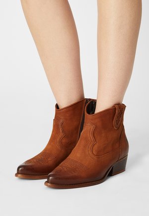 Braune Leder-Stiefeletten mit detaillierter Naht, spitzer Zehenpartie, seitlichem Reißverschluss und niedrigem Blockabsatz. Glatte Textur mit getragenem Aussehen.