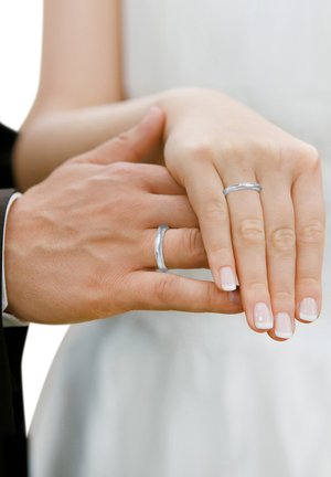 Two hands clasped, showcasing two simple silver rings. One ring has a smooth surface; the other features a textured design. Nails are neutrally polished.