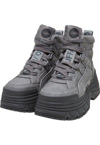 Sneaker alte grigie realizzate in materiale resistente, con suola nera spessa, lacci e dettagli di marca sulla linguetta e sui lati.