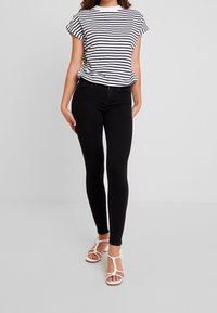Jeans skinny neri abbinati a una T-shirt a righe bianche e blu navy. La T-shirt presenta maniche a cappuccio e l'outfit è completato da sandali bianchi.