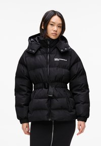 Schwarze Daunenjacke mit tailliertem Bund, hoher Kragen und Reißverschluss. Verfügt über eine glänzende Oberfläche und gestepptes Muster zur Isolierung.