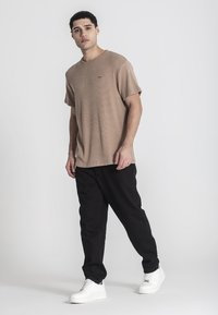 Svetlohnedé rebrované tričko, voľný strih, krátke rukávy. Skombinované s čiernymi nohavicami a bielymi teniskami. Jednoduchý dizajn, bez viditeľných log.