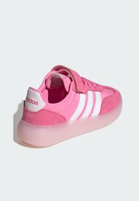 Růžová sportovní bota s suede a syntetickým svrškem, která má tři bílé pruhy, suchý zip a průhlednou gumovou podešev.