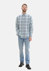 Svetlo modra karo srajca s črnimi in belimi detajli, v kombinaciji s svetlo modrimi jeans hlačami in črnimi čevlji. Ima žep na prsih in dolge rokave.