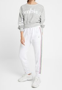 Sudadera gris con el texto "Zombie" en letras blancas. Joggers blancos con rayas de colores a lo largo del costado, combinados con zapatillas deportivas blancas.