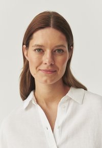 Camicia bianca in lino con botttoni sul davanti e colletto classico, caratterizzata da una superficie leggermente texturizzata e una vestibilità rilassata.