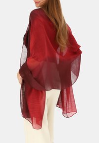Lekki, przejrzysty bordowy szal o płynnym fasonie i miękkiej fakturze, zarzucony na ramiona, z luźnymi krawędziami i luźnym krojem.